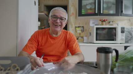 Happy senior man looking at camera smiling in kitchen. Domestic old age lifestyle of scene at home