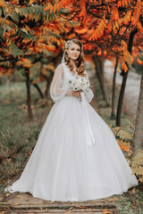 Fototapeta na wymiar full-length portrait in an autumn park. A blonde bride in a wedding dress with sleeves and a bouquet of flowers in her hands