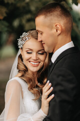 couple in love in the autumn park. Blonde bride in a wedding dress with sleeves. The groom is in a classic black suit, white shirt and tie.