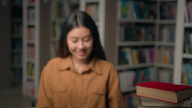 Close-up smiling intelligent asian woman girl student reader reading book in university library read textbook prepare for college exam female portrait concept education camera moving away blurry shot