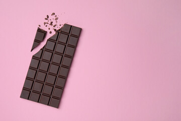 Broken dark chocolate bar on pink background, flat lay. Space for text