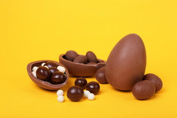 Delicious chocolate eggs and candies on yellow background, closeup