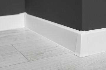 White plinth with connector on laminated floor near black wall indoors, closeup