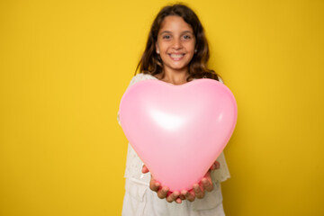 cheerful cute little lady receive birthday present hold heart shaped balloon isolated on yellow color background