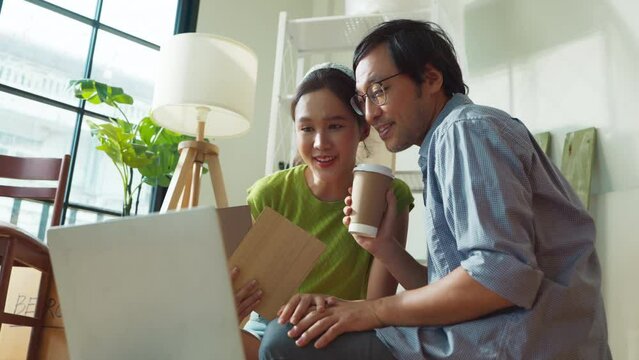Asian Cheerful young marry couple having coffee break sitting among home renovating accessories during the break in new apartment,home relocation renovate interior concept,happiness couple paint wall
