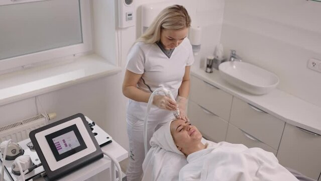 remove facial redness, Professional peeling, Ultrasound cosmetology. Young woman receiving gentle electric facial massage from beauty electroporation machine, woman at spa clinic receiving stimulating