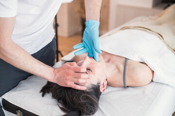 Osteopathic therapist doing treatment to Caucasian woman with jaw problem, mandibular alignment....