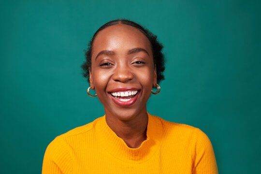 Beautiful Black woman laughs, studio teal background, fashion lifestyle portrait
