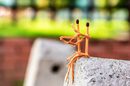 conceptual image of men made of matches sitting, watching the sunset from the edge of a rock. abstract photograph of matches personifying people. concept of people keeping each other company. 