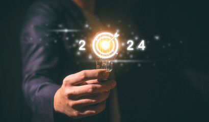 2024 business planning and strategy concept, businessman holding light bulb with the year 2024 target darts, marketing financial and research analysis, investment trends next new year
