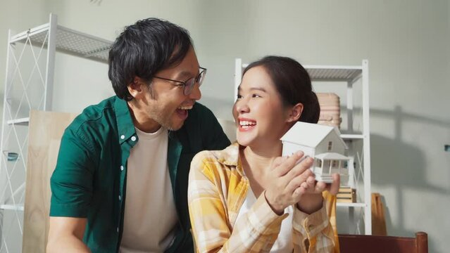 happiness dream home is coming asian sweet marry couple joyful moment hand holding house design model together with full of dream and positive feeling future  while sit talk together at home 