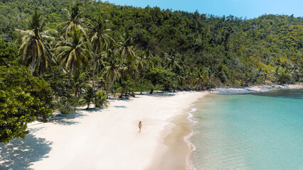 Piękna rajska plaża z białym piaskiem, palmami i turkusową wodą, osoba idąca po wybrzeżu.