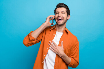 Portrait of overjoyed crazy man speak chatting telephone hand chest laughing isolated on blue color...