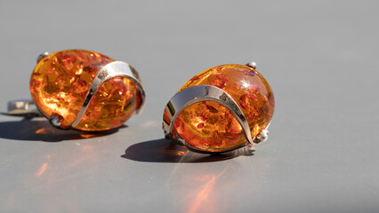 Isolated orange Baltic amber earrings on a gray background. Shiny old amber jewelry in silver....