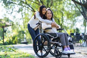 Obraz premium Asian senior woman in wheelchair with happy daughter. Family relationship retired woman sitting on wheelchair in the park age care at retirement home.
