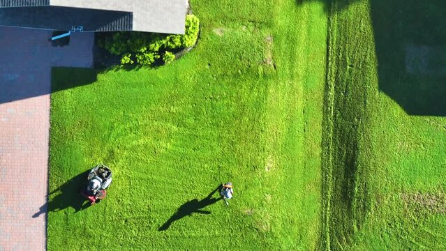Top view of lawn mowing professional service worker cutting grass in summer with a lawn mower vehicle. Landscaping of rural home backyard