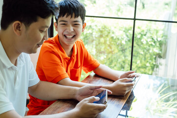 Asian father and son with mobile phone playing games together dad spend time with children family.