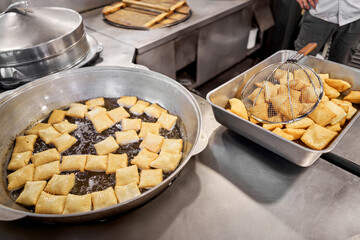 Male cook preparing delicious National Kazakh pastries baursak. street cafe. Fry dough in boiling oil in a frying pan.