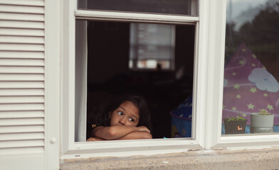 diverse child at home looking out window, lonely bored and sad