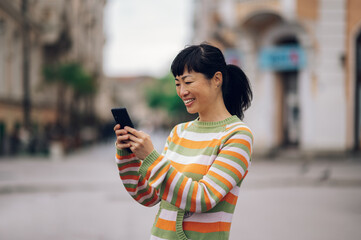 Smiling japanese girl looking at her phone screen while typing a text message.