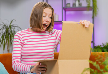 Happy brunette woman unpacking delivery parcel sits at home apartment on sofa. Smiling satisfied...