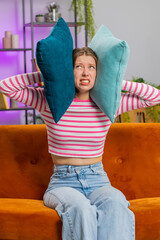 Repair work at neighbours. Irritated woman girl relaxing on couch cover ears with pillows annoyed...