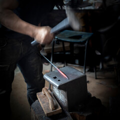 Man in a dark forge workshop forging red hot steel with a hammer on an iron anvil