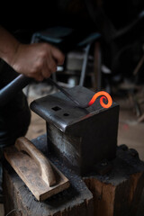 Man in a dark forge workshop forging red hot steel with a hammer on an iron anvil