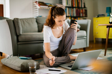 Young woman going over her bills at home while working on the laptop in the living room