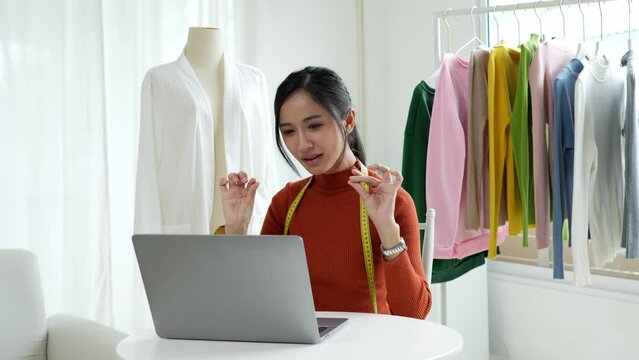 Woman designer entrepreneur showing clothes product on live online social media streaming and packing into cardboard box to preparing for shipping customer delivery at home