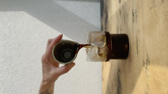 Making iced latte cold coffee. Pouring espresso or cold brewed coffee into a glass filled with ice and adding milk from a bottle. Lifestyle vertical video