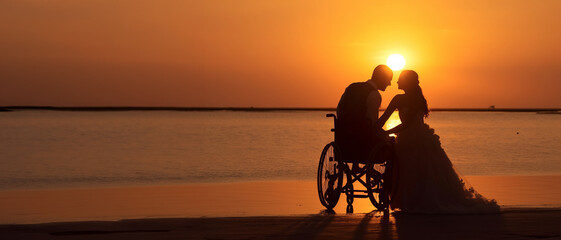 Obraz na płótnie Canvas Man in wheelchair and woman in wedding dress enjoying the sunset on the beach on their wedding day with big copy space left. Banner of newlywed couple on a beautiful beach.