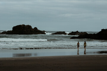 two girls walking to the wild water on dark beach