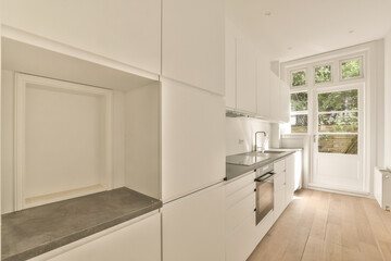 a kitchen with white cabinets and wood flooring in the center of the room is an open door leading to a large window