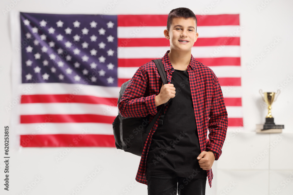 Wall mural Teenage boy with a backpack smiling at the camera in front of USA flag