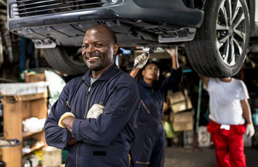 Fototapeta na wymiar Happy black car mechanic standing with armfolded in auto repair with black mechanic woman working underneath car background, Car Mechanic