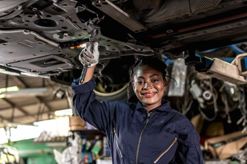 Obraz na płótnie Canvas Smiling black mechanic woman working underneath car in auto repair, Car Mechanic