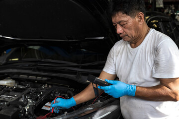Fototapeta na wymiar Asian car mechanic using battery tester in auto repair service, Car Mechanic and maintenance 