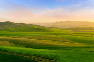 beautiful green valley with green fields with green spring grass with nive hills and mountains and scrnic colorful cloudy sunset on background of landscape