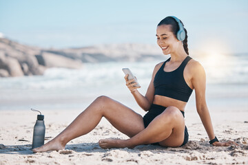 Fitness, break and happy woman relax at beach with phone, music and headphones after training....