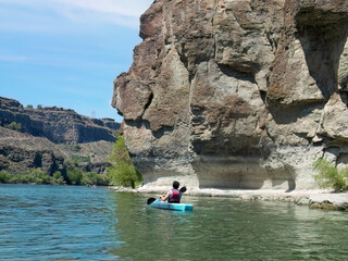 Teenager kayaks by rocky shore.