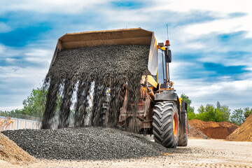 Powerful wheel loader or bulldozer on sky background. Loader pours crushed stone or gravel from the...