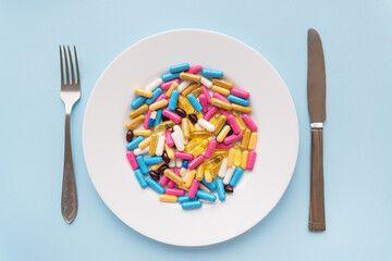 Many multi-colored bright vitamins lie on a plate along with a knife and fork. The concept of...