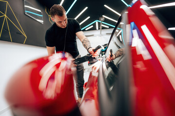 Professional vehicle polishing and detailing service in a modern car workshop. Brightly lit workspace with large led lights. High quality car valeting concept.