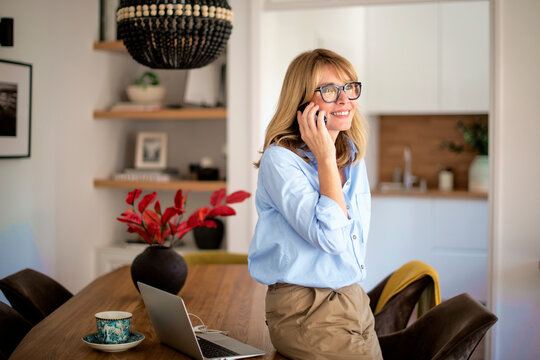 Attractive mid aged woman standing in a modern home and making a call