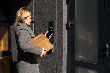 Smart home concept - close up of woman with box use mobile phone to open electronic lock