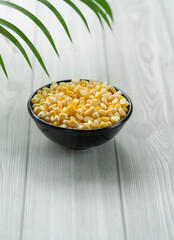 High quality corn seeds on a black bowl isolated on white wooden table