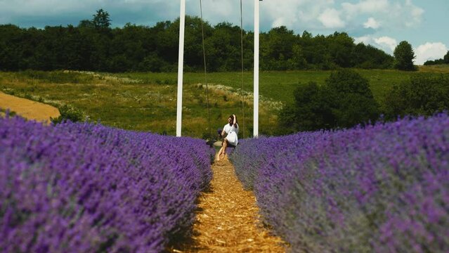 Beautiful free young woman on a swing among bright and fresh lavender on a field. The beauty enjoys her mood and nature.