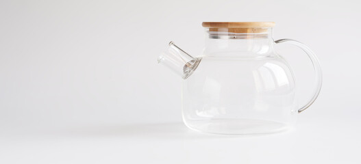 A transparent teapot made of tempered glass with a wooden lid and a metal spiral strainer on a white background. Element of modern trendy kitchen interior