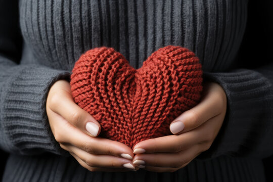 Women's hands in a sweater hold a knitted heart. AI generative.
